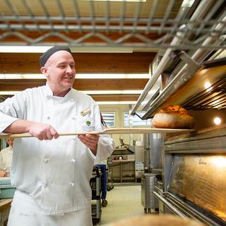 A baking students putting bread in a commercial oven. 
