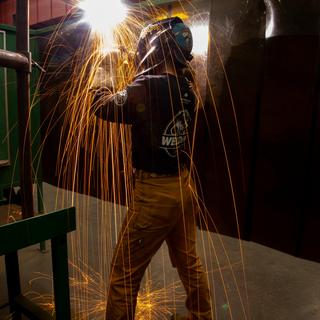 Orange sparks fly over a welding student as they work. 