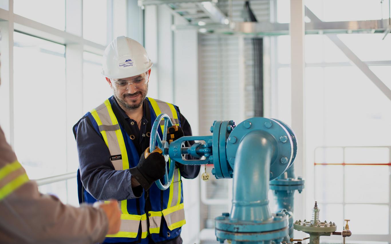 A man in safety gear working on large pipes. 