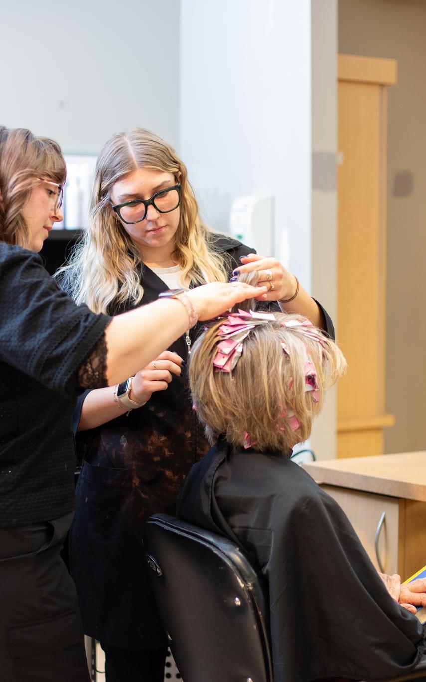 Three VIU hairdressing students dressed in black uniforms apply foils to a customers hair