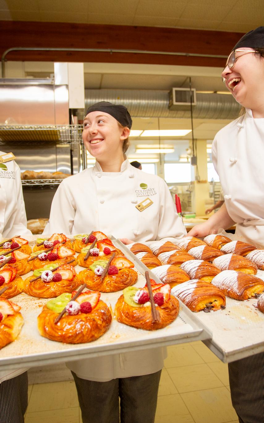 Three baking students show off their pastries and are laughing and smiling